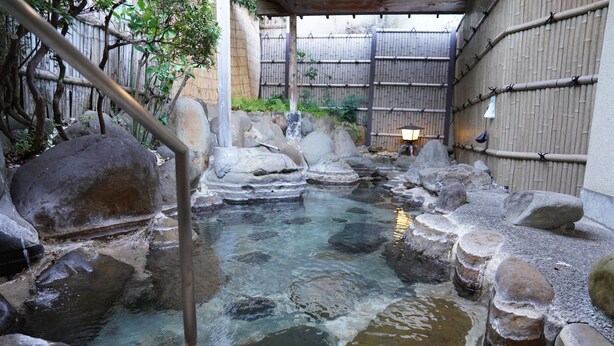 Een traditioneel Japans onsen met een heldere warmwaterbron, omringd door rotsen en een bamboomschutting.