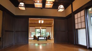 Een traditionele Japanse kamer met tatami vloerbedekking, een lage tafel met kussens en schuifdeuren die uitkomen op een tuin.