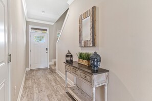 A hallway with a white door, a console table with decorative items, and a rustic mirror on the wall.