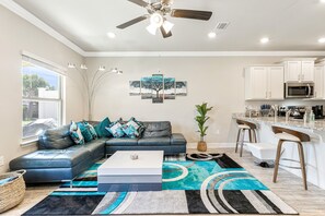A modern living room with a sectional sofa, a coffee table, and a kitchen area with white cabinets and a microwave.