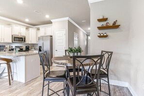 A modern kitchen with white cabinets, a granite countertop, a stainless steel refrigerator, and a dining area with a round table and chairs.