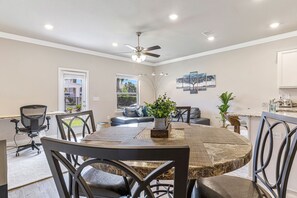 Un espace repas comprenant une table ronde, des chaises, un ventilateur de plafond, ainsi qu’un coin cuisine avec un plan de travail et un évier.