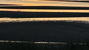 Un atardecer sobre un mar tranquilo con montañas al fondo.