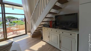 Een moderne woonkamer met een grote televisie, een houten trap en een schuifglazen deur naar een buitenruimte.