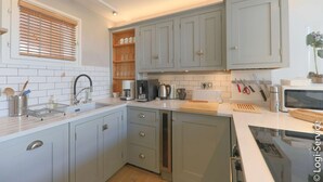 Een moderne keuken met grijze kastjes, een wit aanrechtblad en diverse apparaten, waaronder een koffiezetapparaat en een magnetron.