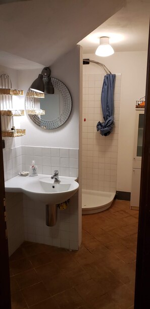 Un baño con lavamanos blanco, espejo, ducha y toallero.