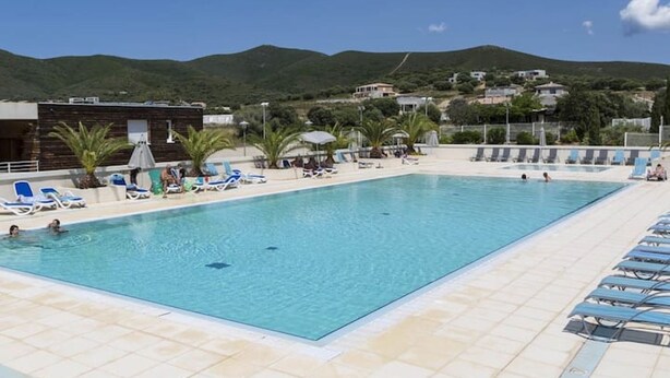 A rectangular swimming pool with clear blue water, surrounded by lounge chairs and umbrellas. - Petite Maison (Belgodère)
