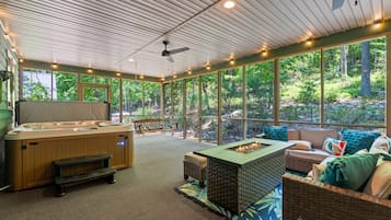 A hot tub, seating area, and large windows overlooking a forested area.