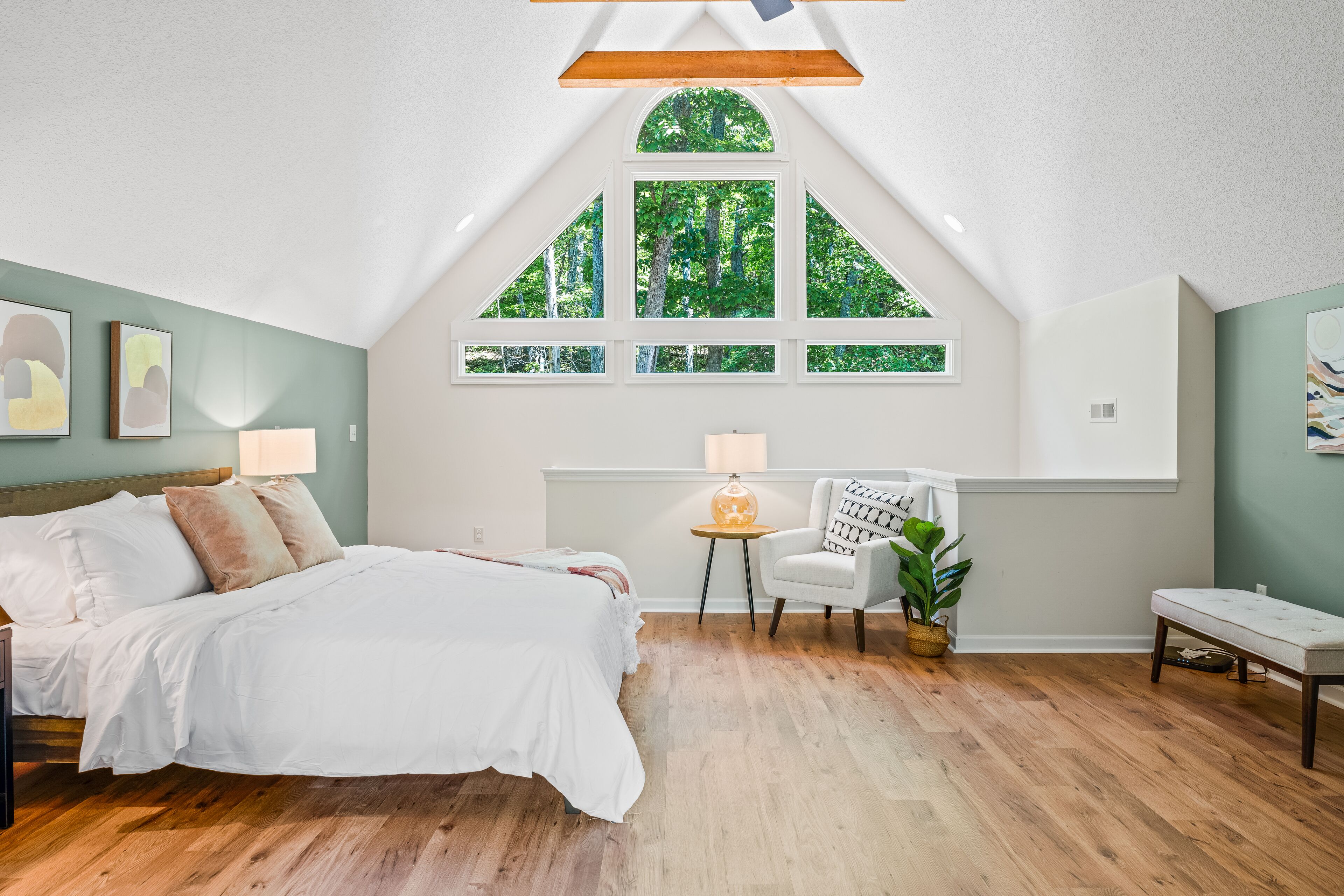 A bedroom with a large bed, a window with a view of trees, a small table, and a chair.