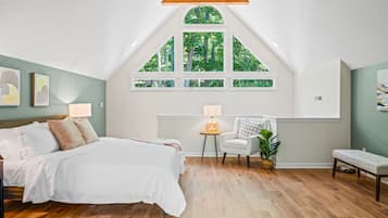 A bedroom with a large bed, a window with a view of trees, a small table, and a chair.