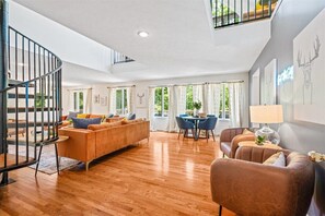 A spacious living area with a wooden floor, a spiral staircase, a dining table with chairs, and a sofa set. - 5BR Modern Mountain Lodge! Hot Tub, FirePit, Games
 (McGaheysville)