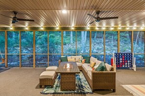 A cozy room with a large window, a sofa, a coffee table, and a ceiling fan. - 5BR Modern Mountain Lodge! Hot Tub, FirePit, Games
 (McGaheysville)