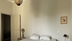 Et soveværelse med seng, natbord, lampe, et billede i ramme og en dør, der fører til en balkon.