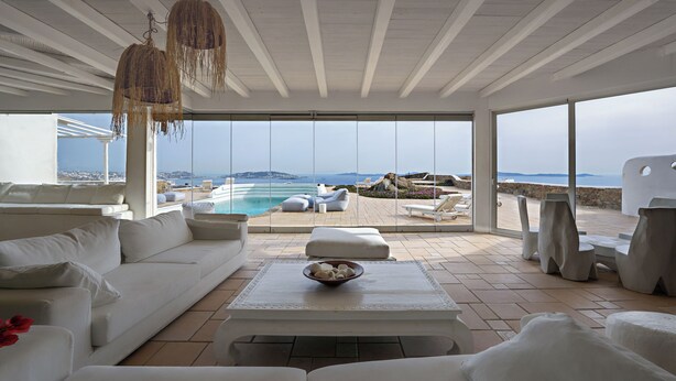 Ein moderner, geräumiger Wohnbereich mit einem weißen Sofa, einem Couchtisch mit einer Schale und Blick auf Pool und Strand.