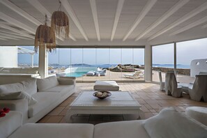 Ein moderner, geräumiger Wohnbereich mit einem weißen Sofa, einem Couchtisch mit einer Schale und Blick auf Pool und Strand.