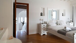 Ein Schlafzimmer mit einem Bett, Nachttischen, einem Spiegel und einer Tür zu einem anderen Raum.