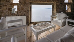 Ein Zimmer mit Steinwänden, weißen Möbeln, Meerblick und einem kleinen Tisch mit dekorativer Verzierung.