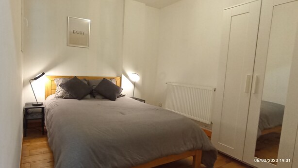 Un dormitorio con cama, lámparas de noche, mesita de noche, armario y un cartel en la pared que dice 'ENJOY'.