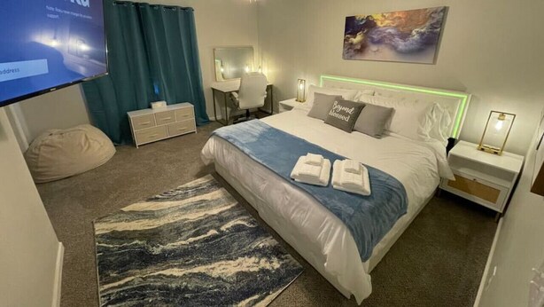 Habitación de hotel con cama, escritorio, silla, televisor y un cuadro en la pared.