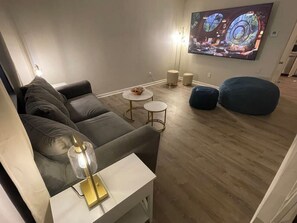 Una sala de estar moderna con un sofá, una mesa de centro, una lámpara y un televisor grande montado en la pared.