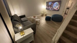 Una sala moderna con un sofá, una mesa de centro y un sillón informal. Un televisor de pantalla plana está montado en la pared.