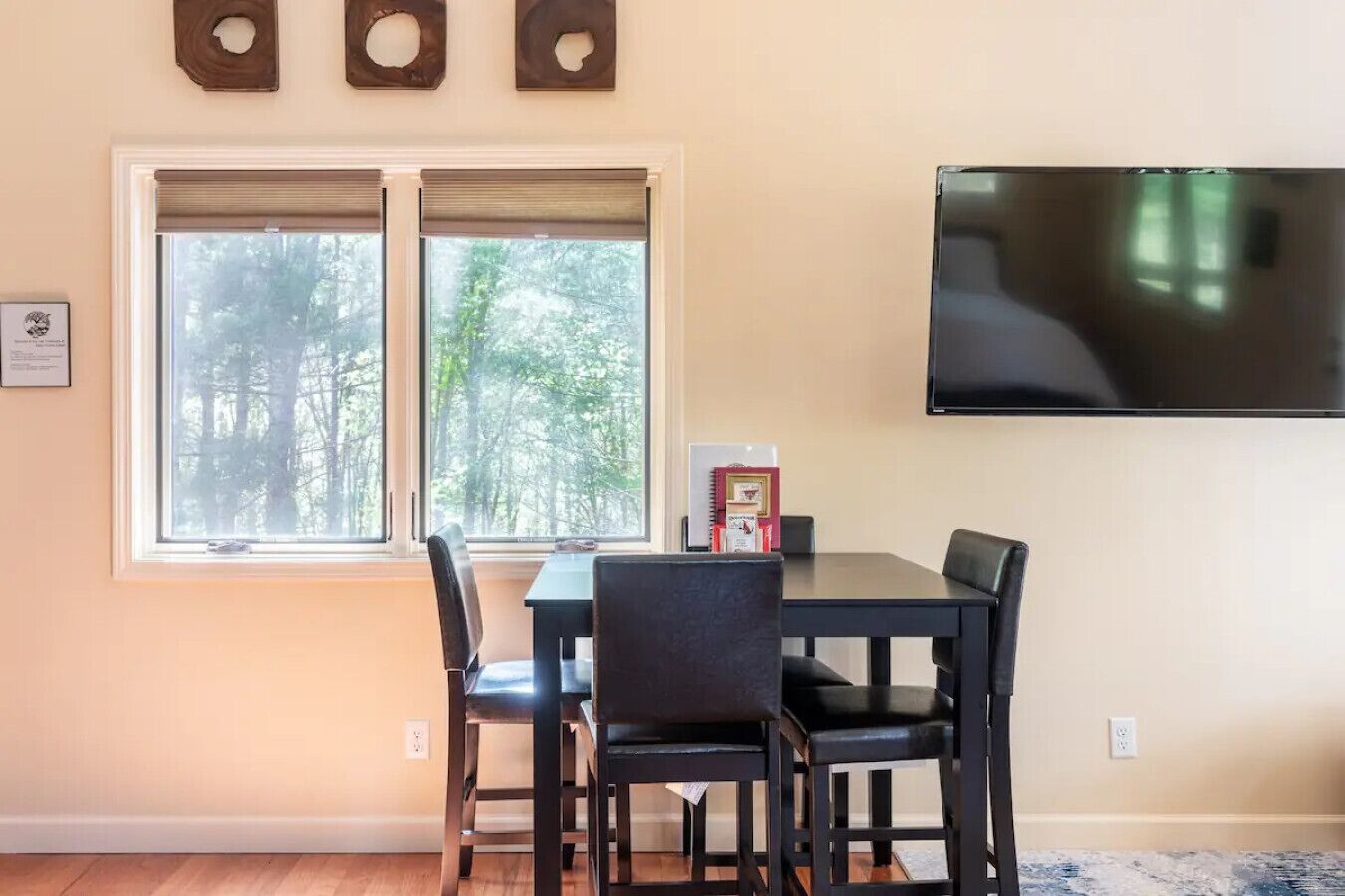 Un coin repas avec une table et des chaises, un téléviseur fixé au mur et une fenêtre avec des stores.