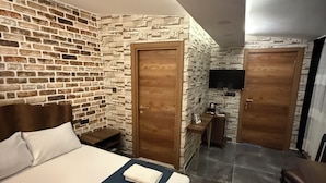 A hotel room with a brick-patterned wall, a large bed with neatly folded towels, a wooden door, a small table with a coffee maker, and a TV mounted on the wall. - La Vien Hotel Old City (Istanbul)