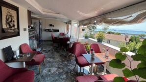 A balcony with red chairs and tables, a ship painting on the wall, and a view of the sea and buildings. - La Vien Hotel Old City (Istanbul)