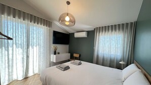 Un dormitorio moderno con una cama grande, una mesita de noche, un televisor montado y una lámpara colgante.