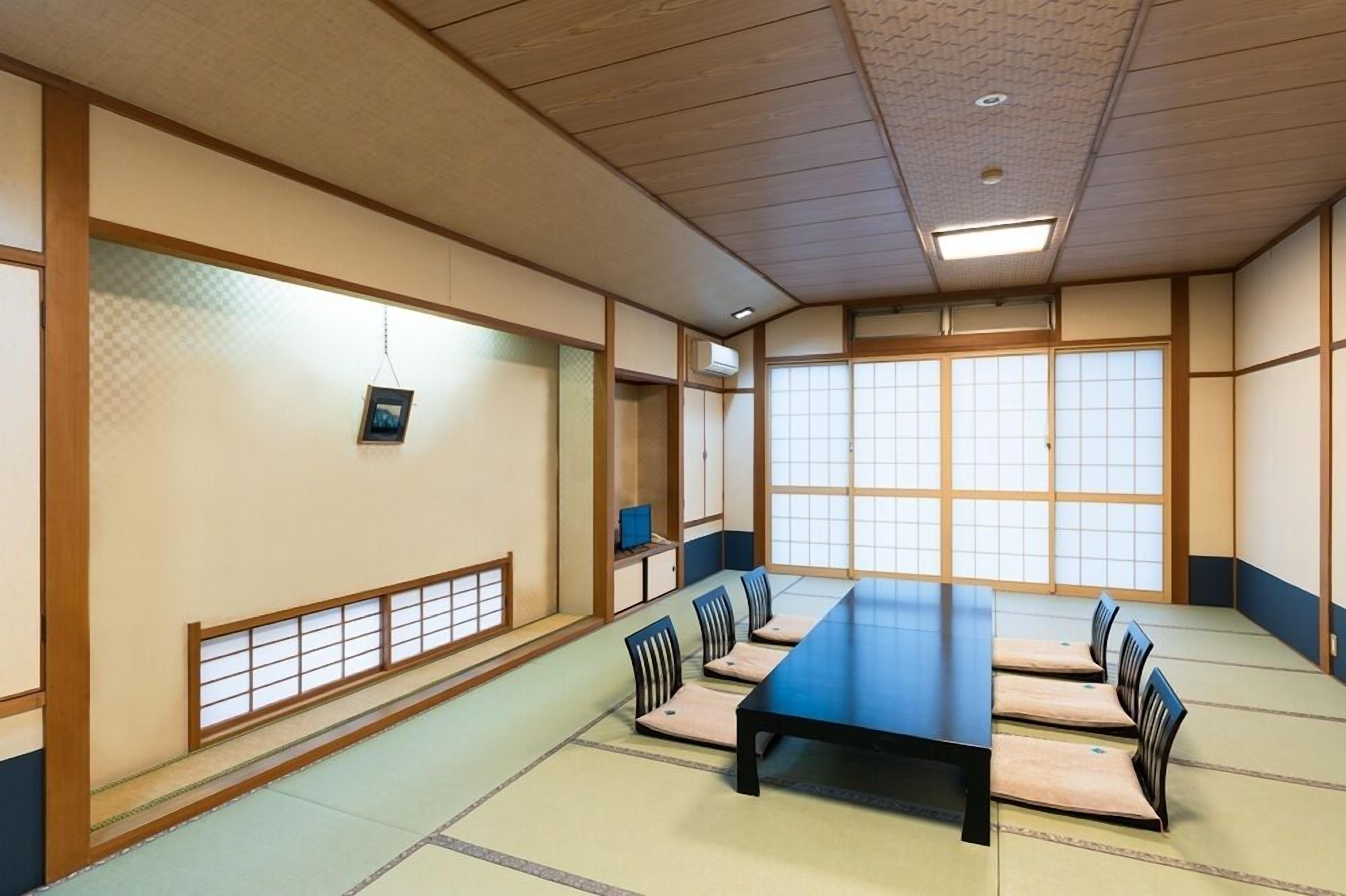 Une pièce de style japonais traditionnel, avec un sol recouvert de tatamis, une longue table et de petites chaises en bois.