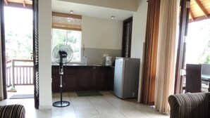 Una sala de estar con un sofá, una mesa de centro, un ventilador y un área de cocina con un refrigerador y una cafetera.