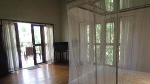 Una habitación con suelo de madera, una cama con dosel, un televisor y un ventanal corredero que da a un espacio exterior.