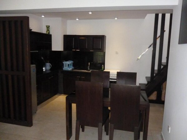 Una cocina compacta con armarios oscuros, una mesa de comedor con sillas y una escalera que sube a otro nivel.