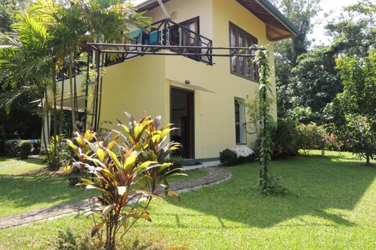 A two-story house with a balcony, surrounded by a well-maintained garden and trees.