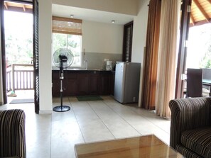 A living room with a sofa, a coffee table, a fan, and a kitchen area with a refrigerator and a coffee maker. - The Residence Bentota (Bentota)