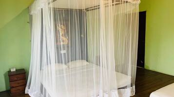Una camera con un letto sotto una tenda bianca, un comò di legno e una parete verde.