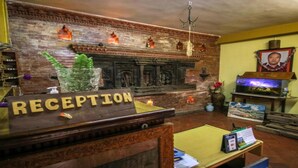 A reception area with a wooden reception desk labeled "RECEPTION," a brick wall with decorative elements, a chandelier, and a framed portrait on the wall. - MeroStay 155 GGH (Bhaktapur)