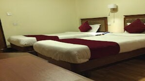 A hotel room with two single beds, each with a red pillow and white bedding. There is a wooden nightstand with a lamp on it. - MeroStay 155 GGH (Bhaktapur)