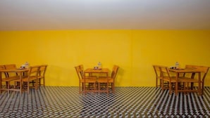 A room with three wooden tables and chairs against a yellow wall, with a checkered floor pattern. - MeroStay 154 White & Peace (Lalitpur)