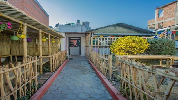 A narrow pathway flanked by bamboo fences and potted plants, leading to a building entrance. - MeroStay 154 White & Peace (Lalitpur)