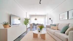 A modern living room with a sofa, coffee table, and TV. There is a dining area with chairs and a table in the background. - iloftmalaga Playa Machado (Málaga)