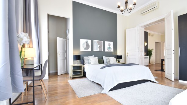 Ein modernes Schlafzimmer mit einem großen Bett, einem Schreibtisch und einem Stuhl. Über dem Bett hängen drei Wandbilder.