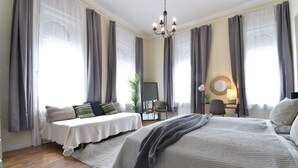 Ein Schlafzimmer mit einem großen Bett, einem Einzelbett, einem Schreibtisch mit Stuhl, einer Pflanze und einem Spiegel an der Wand.