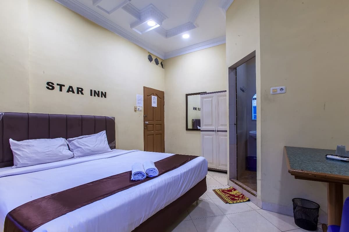 Hotellihuoneessa on sänky, työpöytä ja peili. Huoneessa on ovi ja seinä, jossa on kyltti, jossa lukee: ”STAR INN”.