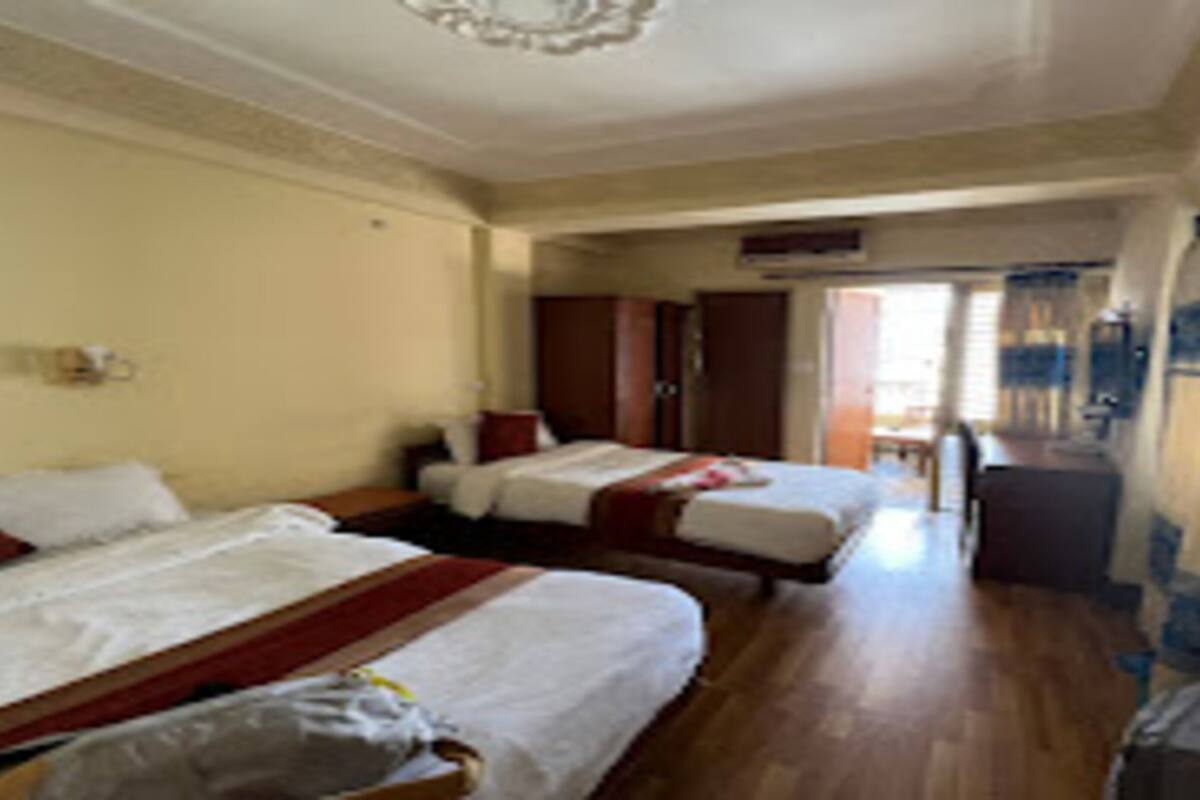 A hotel room with two beds, a wooden floor, a ceiling with a decorative light fixture, and a view of the outside through a door.