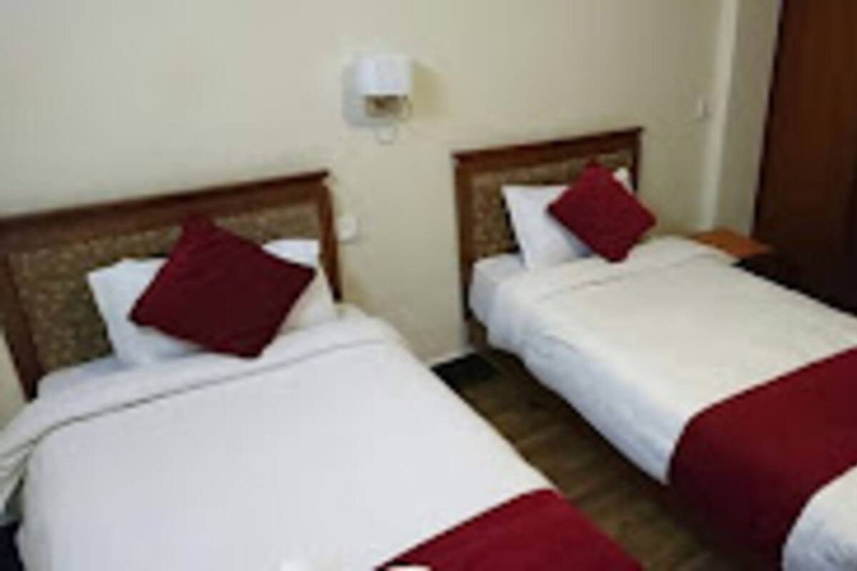 A hotel room with two single beds, each with a red pillow and white bedding.