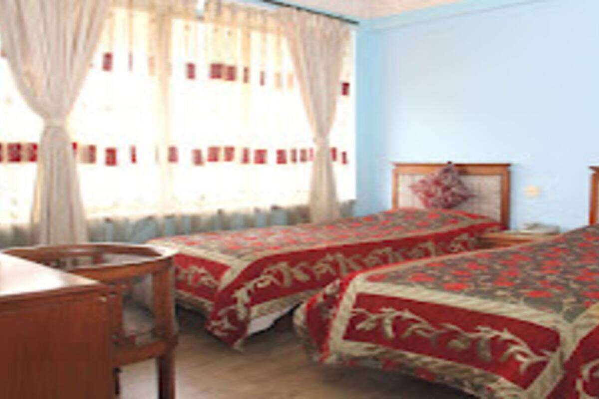 A room with two single beds, a wooden desk, and a window with curtains.