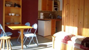 A compact kitchen with wooden cabinets, a microwave, and a coffee maker. There is a dining table with chairs and a small sofa in the living area. - Studio cabin for 4 with parking in Crest-Voland (Crest-Voland)