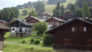 A cluster of traditional wooden houses with sloped roofs, surrounded by greenery and set against a hilly backdrop. - Studio cabin for 4 with parking in Crest-Voland (Crest-Voland)