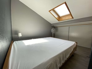 Quarto com claraboia, cama, mesa de cabeceira, abajur e ventilador.